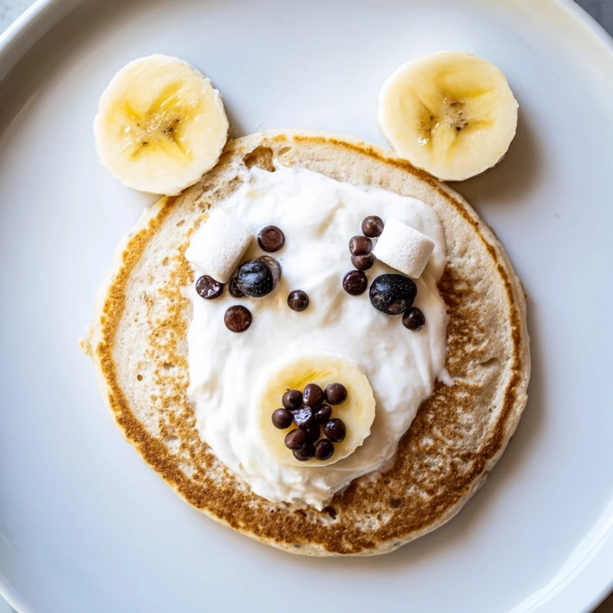 Close-up of a delightful Polar Bear Pancake Stack, featuring chocolate eyes and fruit accompaniments on a wooden board.