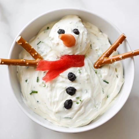 Creamy Melted Snowman Dip, complete with a carrot nose and pretzel arms, ready to dip.