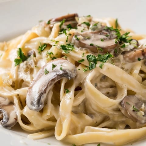A bowl of Creamy Mushroom Alfredo pasta garnished with fresh parsley and grated Parmesan cheese.