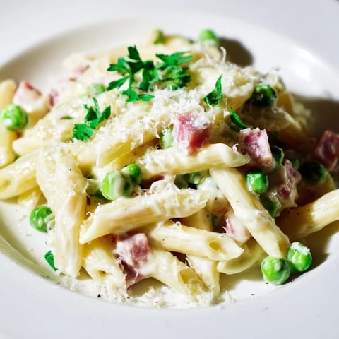 Forkful of Spring Pea & Ham Pasta shows al dente penne, sweet peas, and savory ham in a velvety cream sauce.  