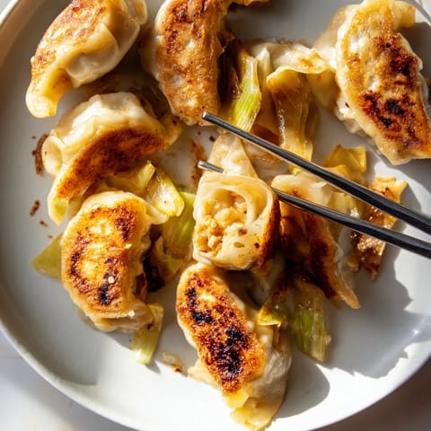 Crispy smashed gyozas plated with a small bowl of soy-vinegar dipping sauce and chili oil. A sprinkle of green onions and sesame seeds adds fresh flavor and texture.  